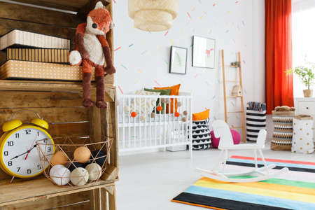 Close-up of plush fox and yellow clock on wooden shelf in colorful child's room with rocking horseの写真素材