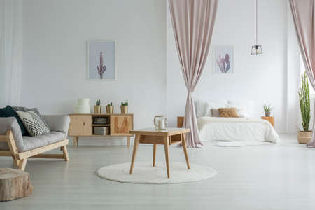 Spacious living room with wooden table on white carpet, rustic cupboard and grey sofa near open...