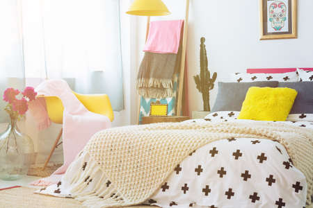 Yellow chair with pink blanket next to king-size bed with yellow pillow and beige blanket in mexican bedroom with cactusの写真素材