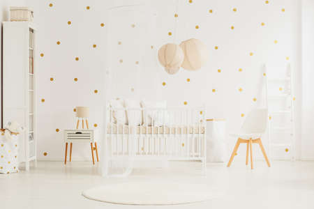 Wooden crib with canopy and pillows in white baby room with dotted wall and lanterns