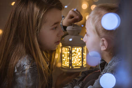 Two young sisters sitting with lantern in the darkの写真素材