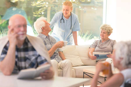 Elderly man asking doctor about his health while drinking tea and senior woman reading newspaperの写真素材