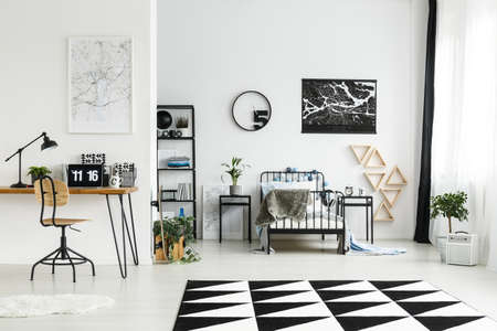 Wooden chair at desk with laptop in workspace in monochromatic boy's bedroom with carpet, round clock and plantsの写真素材