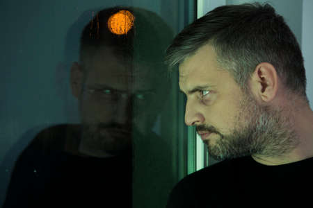 Depressed and lonely man looking through a window during mourning periodの写真素材
