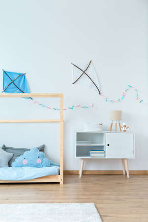 Handmade kites on the wall above white cupboard with lamp and wooden bed with blue bedding in boy's bedroomの写真素材