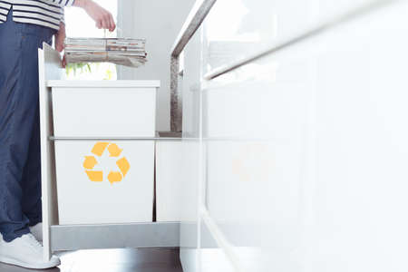 Close-up of eco friendly person sorting paper in the kitchen into recycling container marked with yellow symbolの写真素材