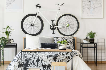White bicycle on bedhead and plants on cabinets in bright teenager's bedroom with book, clock and vaseの写真素材
