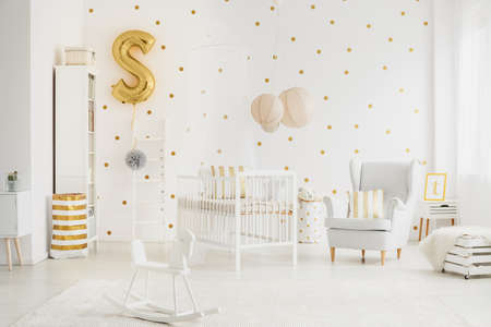 Three big, beige lampshades hanging above bed for baby in bedroom with dotted wallの写真素材