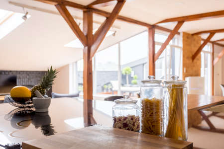 Pastas in glass containers next to wooden board on glossy countertop with fruits in bowlの写真素材