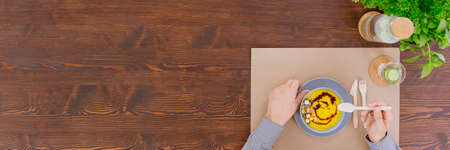 High angle of a man eating pumpkin soup with croutons on wooden table