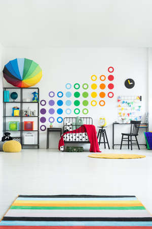 Colorful carpet in scandi child's room with toys and black chair at desk near bed against a wall with stickersの写真素材