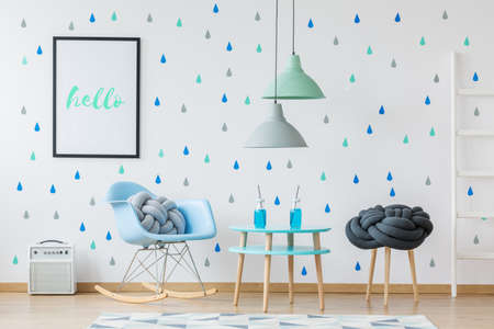 Glass bottles on a table under lamps in designer kid's room with blue rocking chair and posterの写真素材