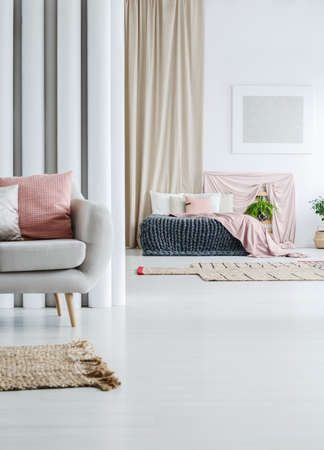 Beige curtain in multifunctional loft with grey sofa and pink coverlet on king-size bedの写真素材