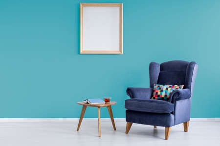 Book with blue cover and cup of tea on small table in reading room with armchairの写真素材