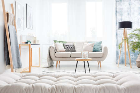 Grey mattress and ladder in bright living room with beige settee, table and lampの写真素材