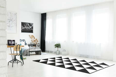White spacious boy's bedroom with black and white carpet and wooden chair at desk with computerの写真素材