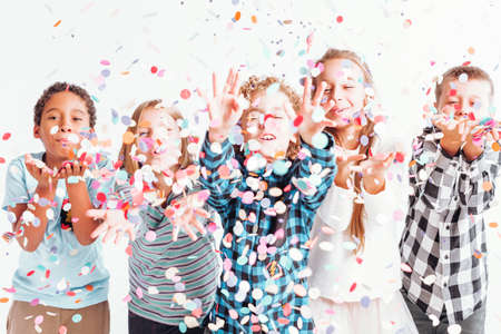 Group of joyful kids merrily blowing colorful confetti into the airの写真素材