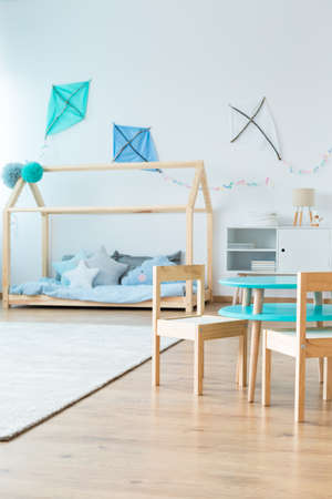 Small wooden chairs at table in scandinavian style kid's bedroom with kites on the wall above bed