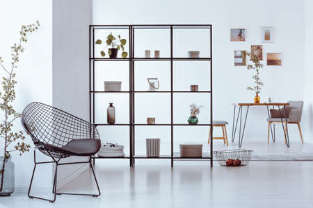 Black metal rack with books, plants, candles and decorations standing in a white room with metal chairの写真素材