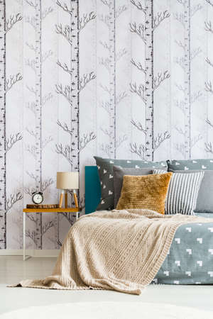 Beige blanket on king-size bed in simple bedroom with lamp and clock on nightstand