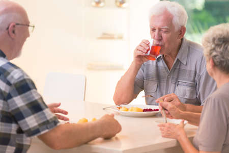 Elderly man drinking juice while sitting at a table in the canteen with friends