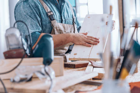 Close-up of carpenter checking quality of wooden board at desk with equipmentの写真素材