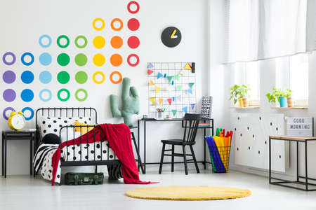 Yellow clock on black cabinet and desk with chair near bed in colorful kid's bedroomの写真素材