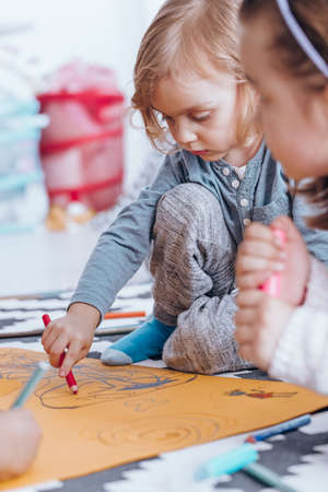 Young boy drawing on orange paper with his classmate in nursery schoolの写真素材