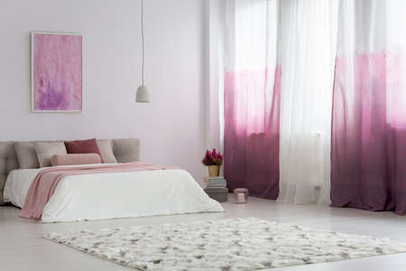 Gradient curtains in bright bedroom with patterned carpet and pink painting on the wall above bedの写真素材