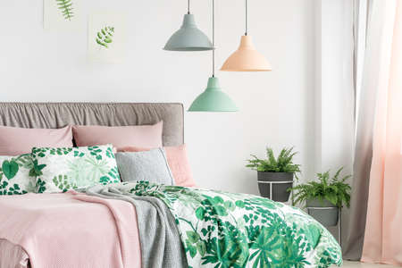 Three lamps in pastel colors hanging above bed with soft bedhead in bright interiorの写真素材