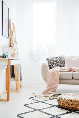 Pink blanket on beige sofa and pouf on patterned carpet in daily room with console tableの写真素材