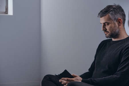 Man looking at his phone, sitting alone in the corner of hospital roomの写真素材