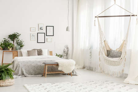 Small white lampshade hanging in bright room with hammock, king size bed and postersの写真素材