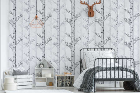 White wooden house shaped box with shelves standing next to pallet chest in bright kid's room