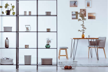 Twig in a glass vase standing on a wood and metal hairpin table in white dining room with photos on the wallの写真素材