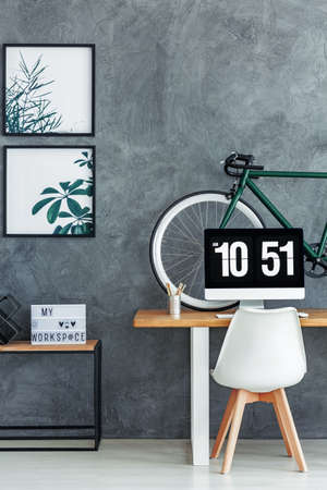 Living room with grey raw wall and simple workspace with bike placed on deskの写真素材