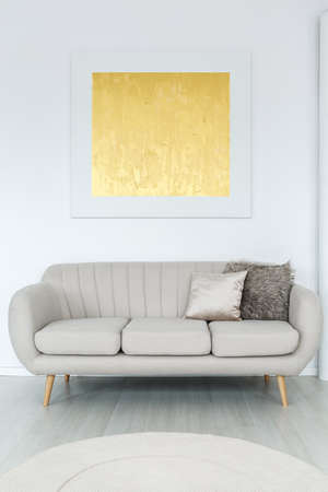 Gold modern poster hanging on white wall above grey couch with pillows in room with rugの写真素材