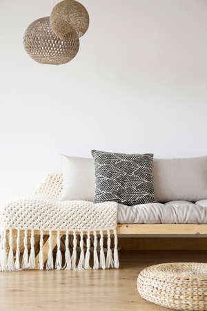 Patterned blanket on wooden bed, pouf and lamps in bright bedroom with copy space on white wall