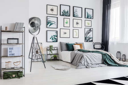 Green suitcase lying under black metal rack with books, candle and decorations in white bedroomの写真素材