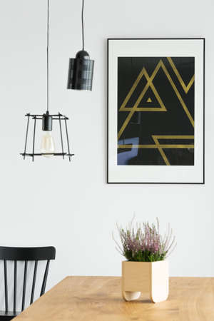 Close-up of black and gold triangle poster and industrial lamps above wooden table with lavenderの写真素材