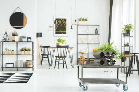 Metal industrial coffee table standing in the middle of white dining room with modern wine holder on...