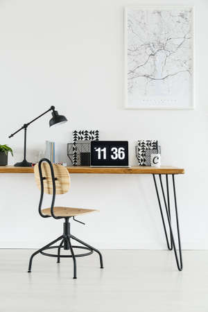 Laptop with clock on screensaver placed on hairpin desk standing under a poster hanging on white wallの写真素材