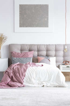 Silver abstract painting above cozy king-size bed in stylish interior of hotel room with gray headboard, white sheet and pink bedcoverの写真素材