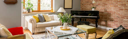 Flowers in vase on glass table in classic living room with white sofa and black piano against brick wallの写真素材