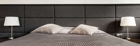 Closeup shot of two bedside lamps on both sides of a large bed with a wall mounted headrestの写真素材