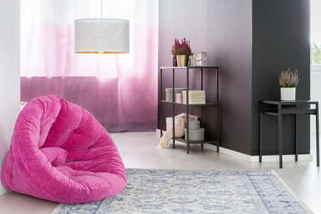 Pink pouf on patterned carpet in elegant room with lamp and plants against black wallの写真素材