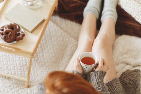 Young woman sitting by a breakfast tray on a bed holding a cup of tea in her handsの写真素材