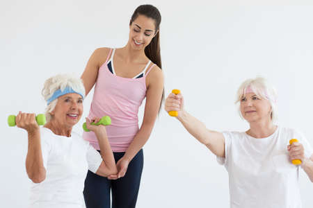 Trainer helping two elder ladies during arms training with dumbbellsの写真素材