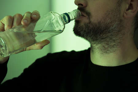 Middle-aged alcoholic with beard drinking transparent liquor from a bottleの写真素材