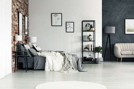 Spacious bright bedroom with drawings on the wall and decorations on shelves near sofa and lampの写真素材